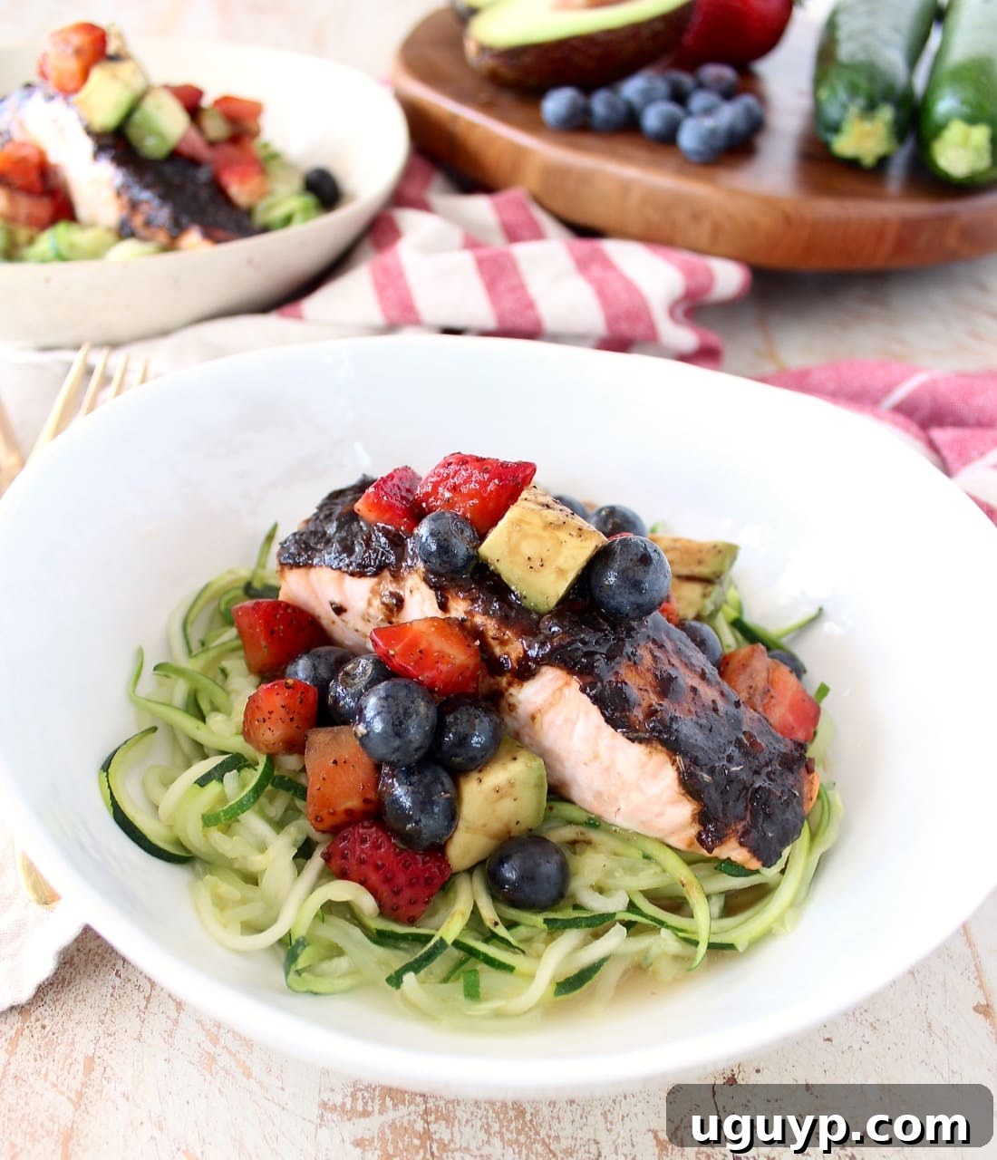 Roasted balsamic salmon is served over zucchini noodles topped with a colorful berry avocado salsa in a white bowl, presenting a flavorful, easy, gluten-free, dairy-free, and Whole30-approved meal.