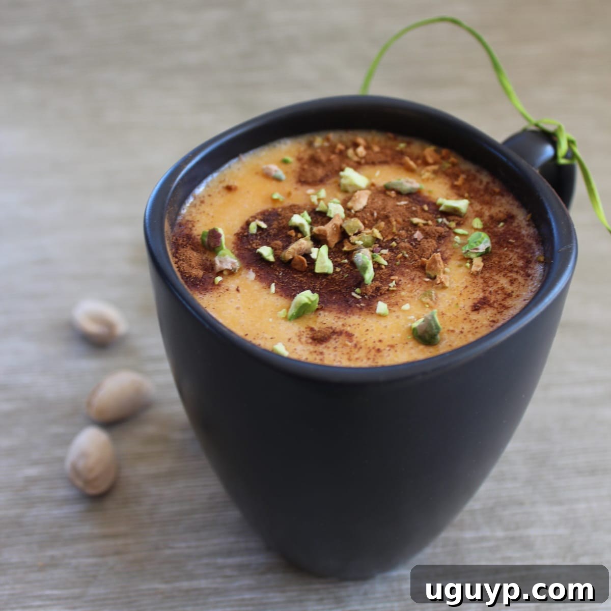 A warm, inviting Korean Goguma Green Tea Latte topped with cinnamon and pistachios in a white mug.
