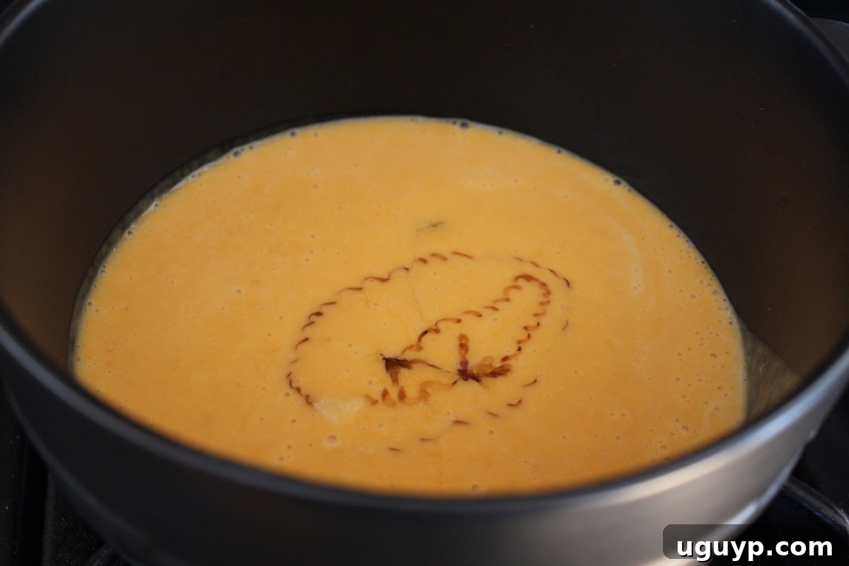 Sweet potato and milk mixture simmering in a pot on the stove, with honey added for sweetness.