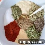 A bowl of separated dried herbs and spices, with a spoon nearby, illustrating the components of the beef stew seasoning before mixing.