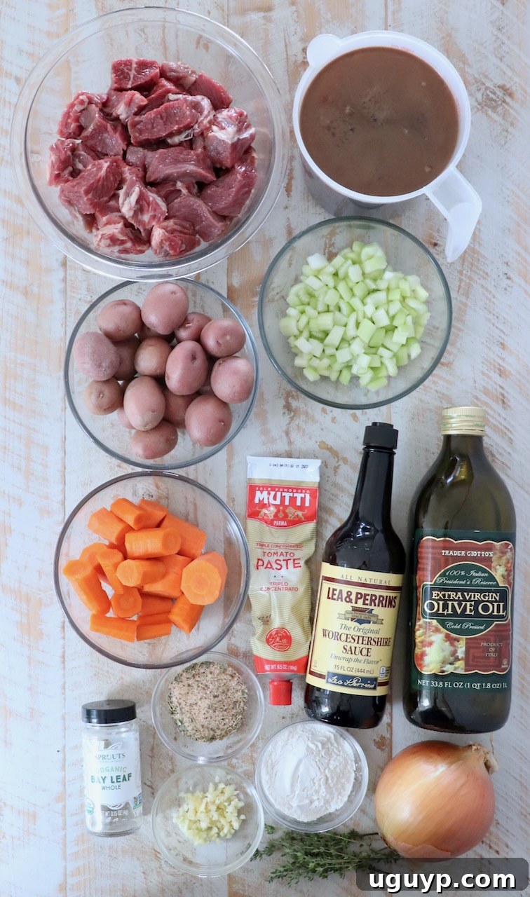 Assorted fresh ingredients for beef stew arranged on a rustic white wooden board.