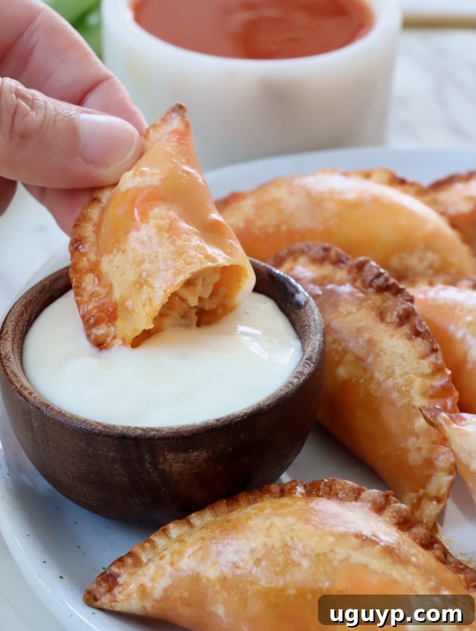 Hand dipping a Buffalo chicken bite in a small bowl of blue cheese dressing, showcasing its crispy texture.