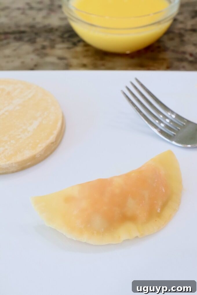 A single uncooked Buffalo chicken bite, perfectly sealed with crimped edges, resting on a cutting board, showcasing its half-moon shape.