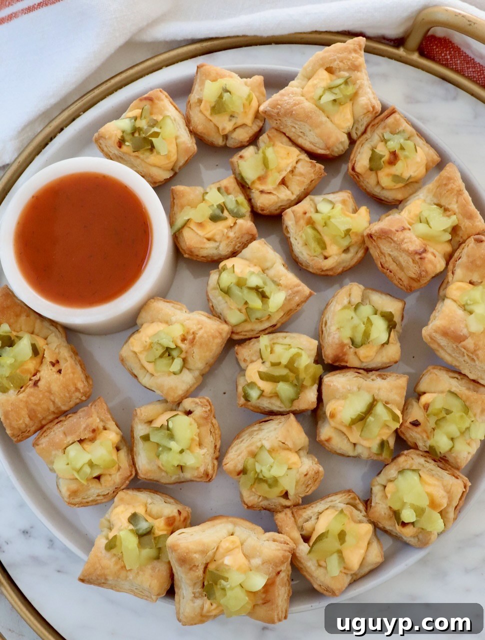 pickle puff pastry bites on a marble board with a small bowl of hot sauce