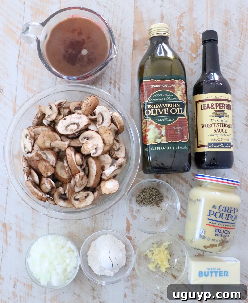 Fresh ingredients for homemade mushroom gravy laid out on a white wooden board, including sliced mushrooms, onions, garlic, and beef broth.