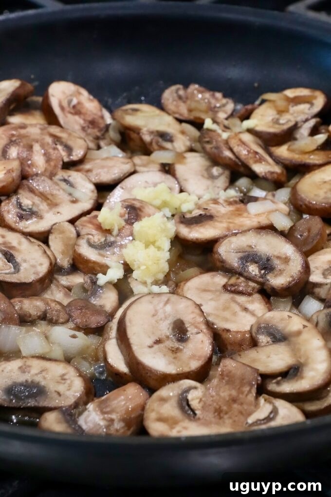 Minced garlic added to the skillet with sautéed mushrooms, intensifying the aroma.