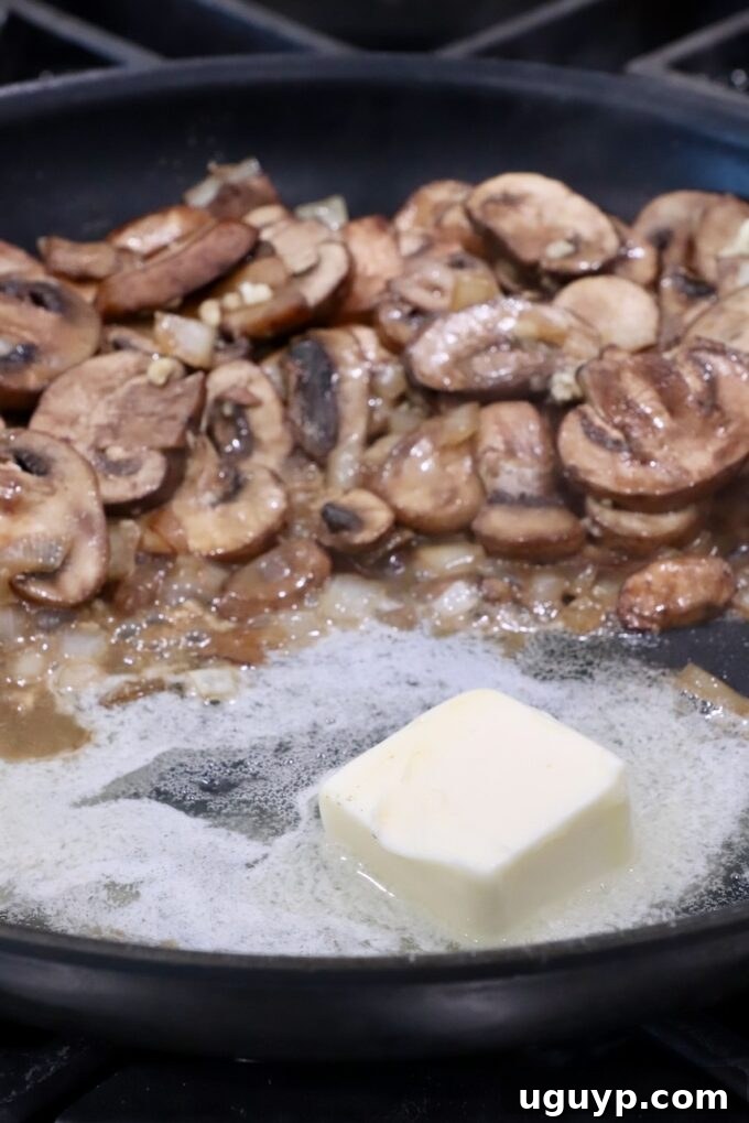 Melted butter combined with the cooked mushrooms in the skillet, forming the base for the roux.