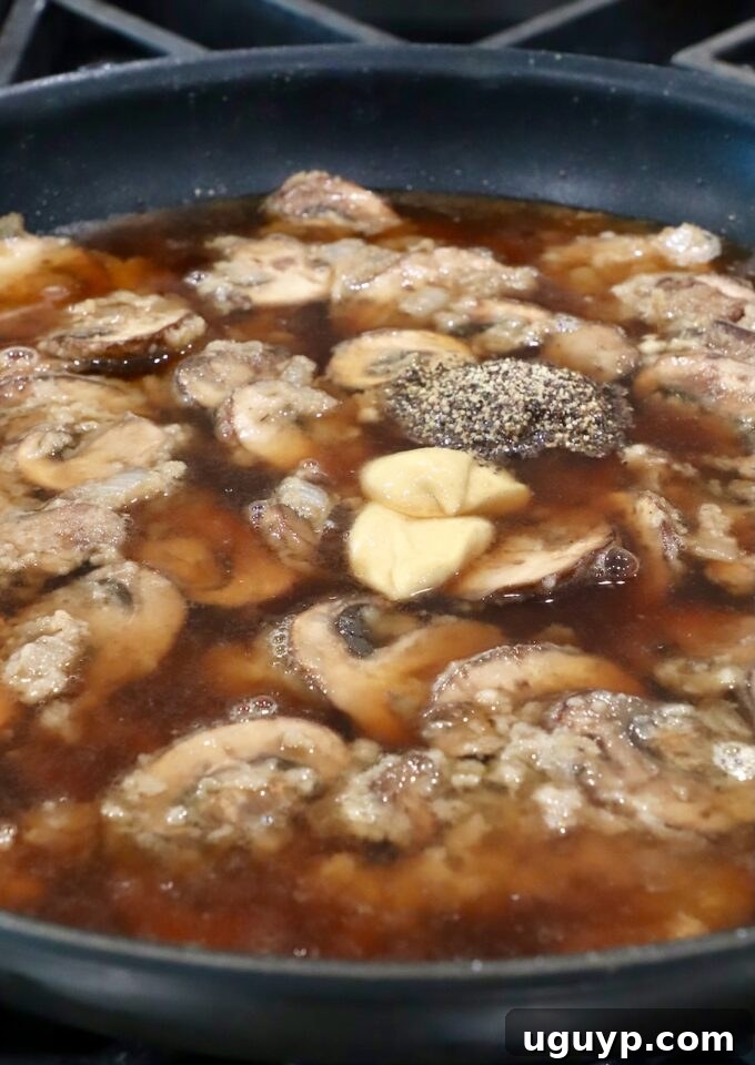 Beef broth being poured into the skillet with the mushroom roux, along with Dijon mustard and black pepper.