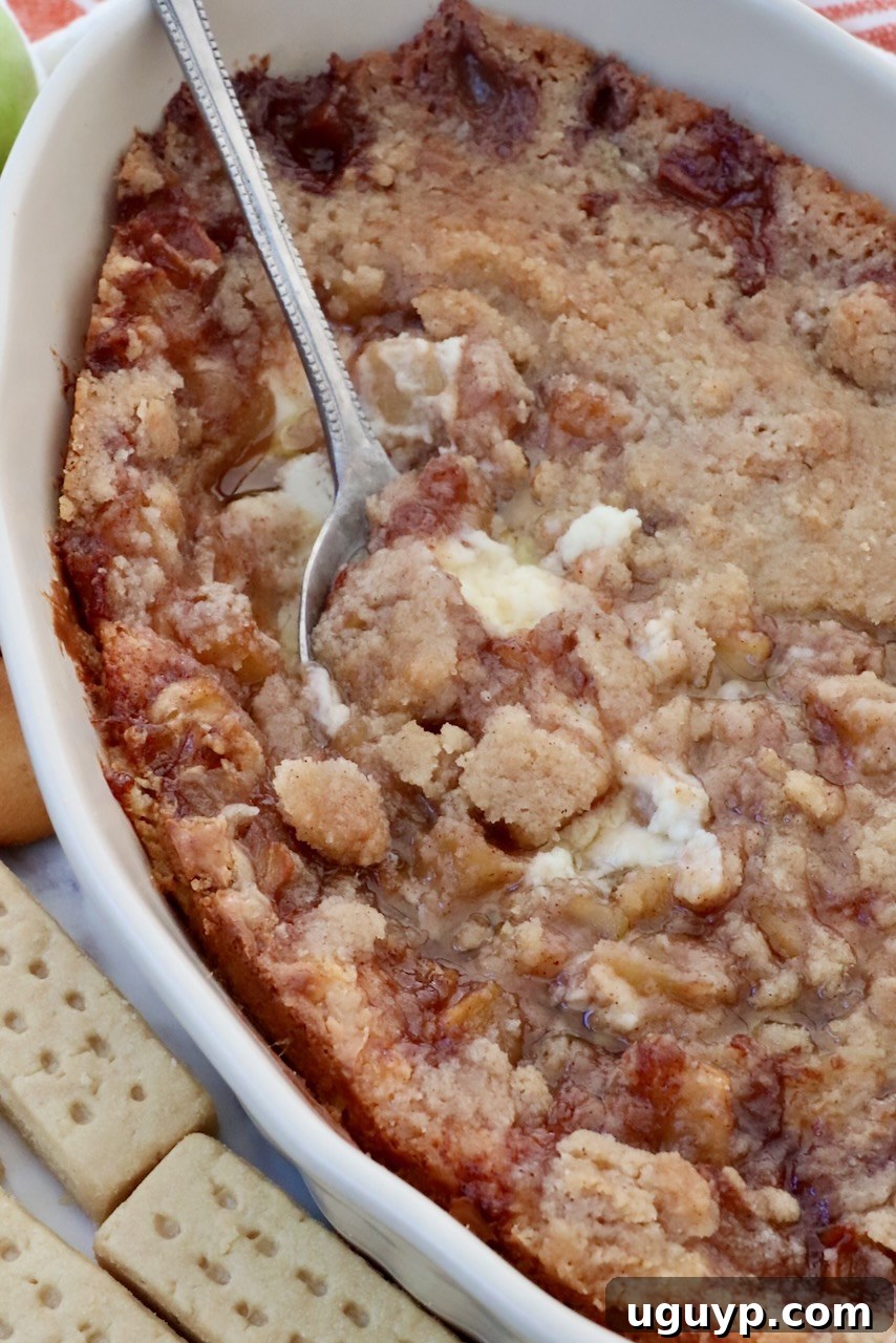 Warm baked apple pie dip in a casserole dish, ready to be served with a spoon nestled in the rich layers.