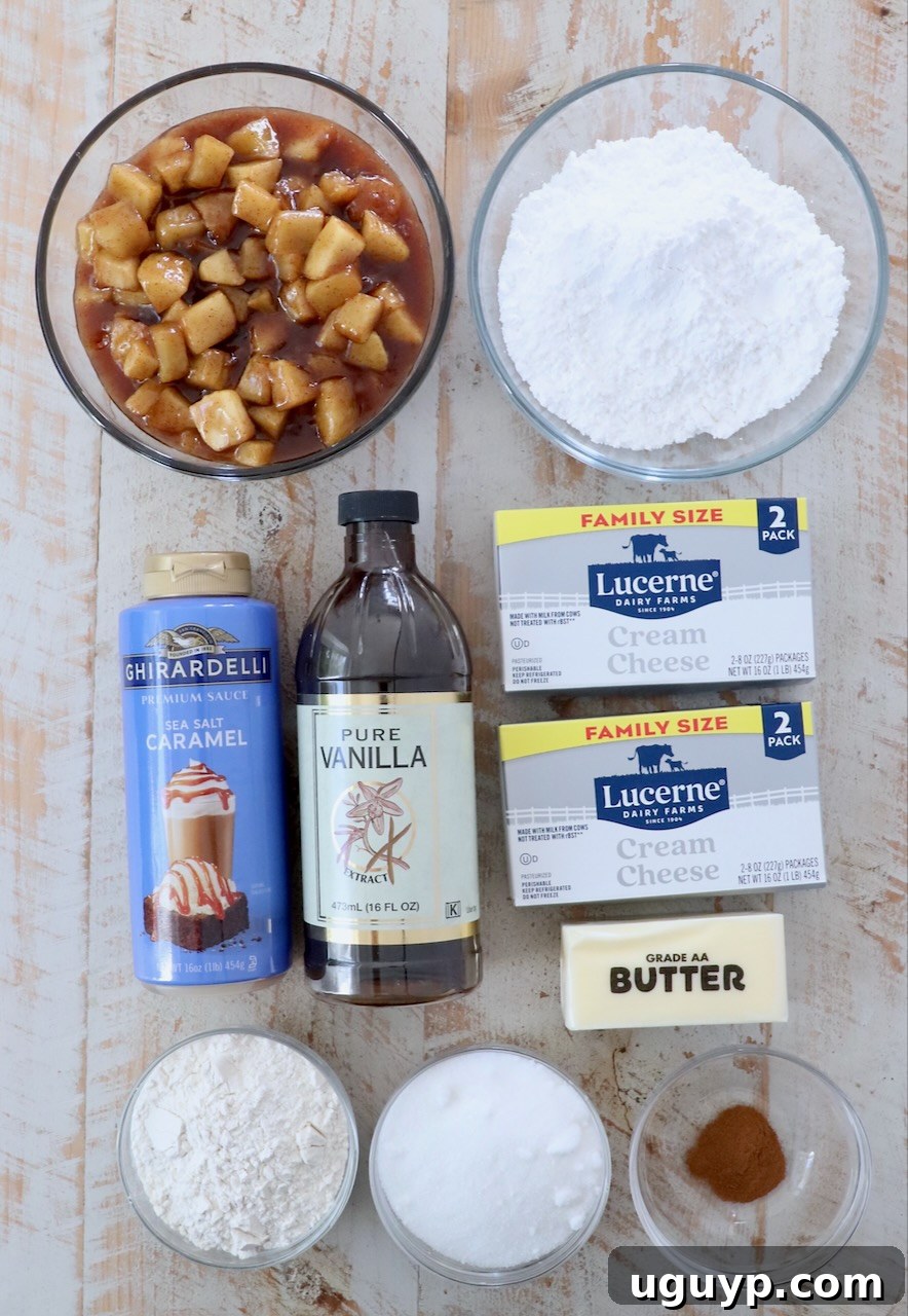 A collection of fresh ingredients for apple pie dip, including cream cheese, butter, apples, and spices, neatly arranged on a rustic white wood board.