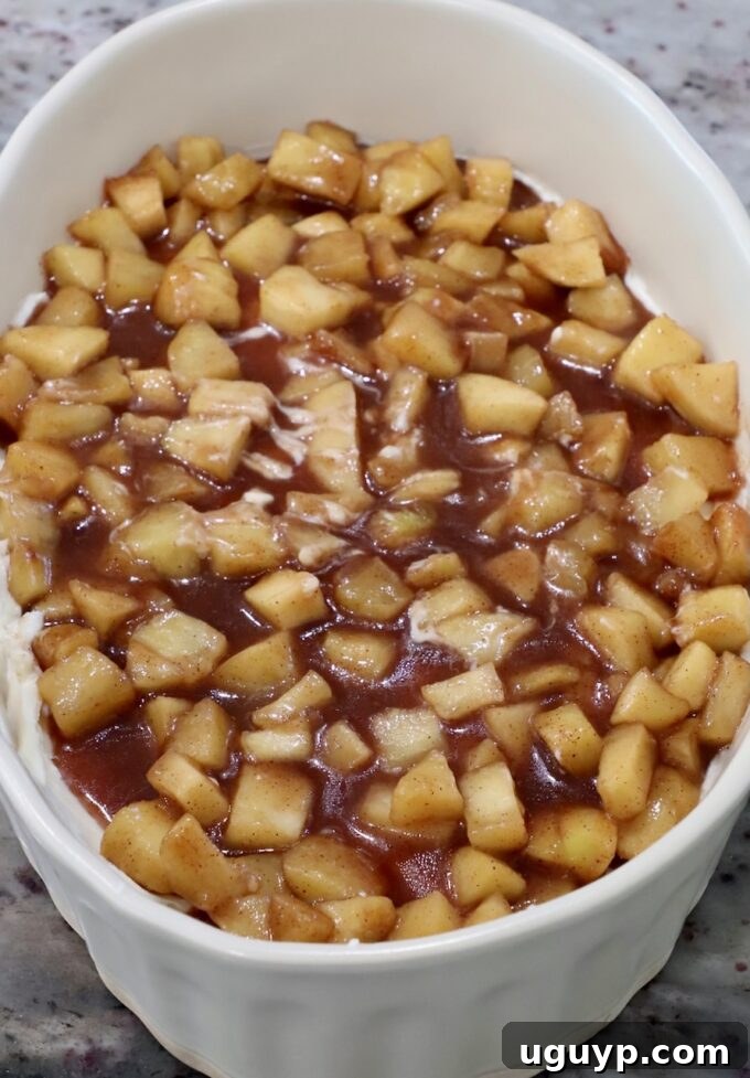 Delicious apple pie filling generously spread on top of the cream cheese layer in a casserole dish, ready for the next step.
