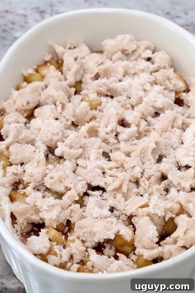 The final layer of cinnamon sugar crumble perfectly covering the apple pie filling in a casserole dish, poised for baking.