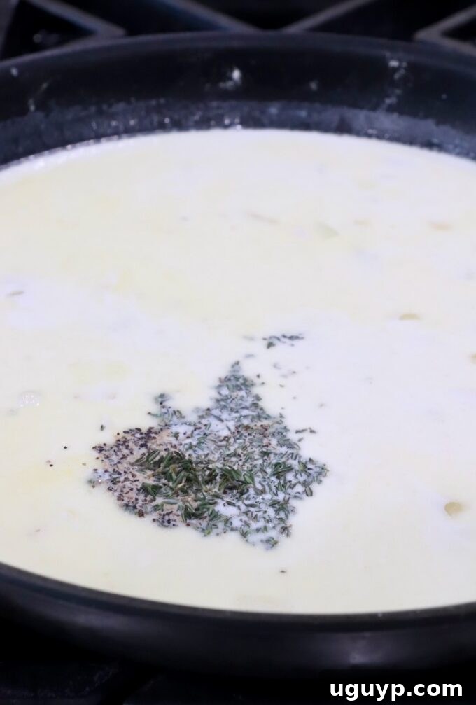 A rich, velvety cream sauce in a skillet, seasoned with black pepper, salt, and fresh thyme, emitting steam.