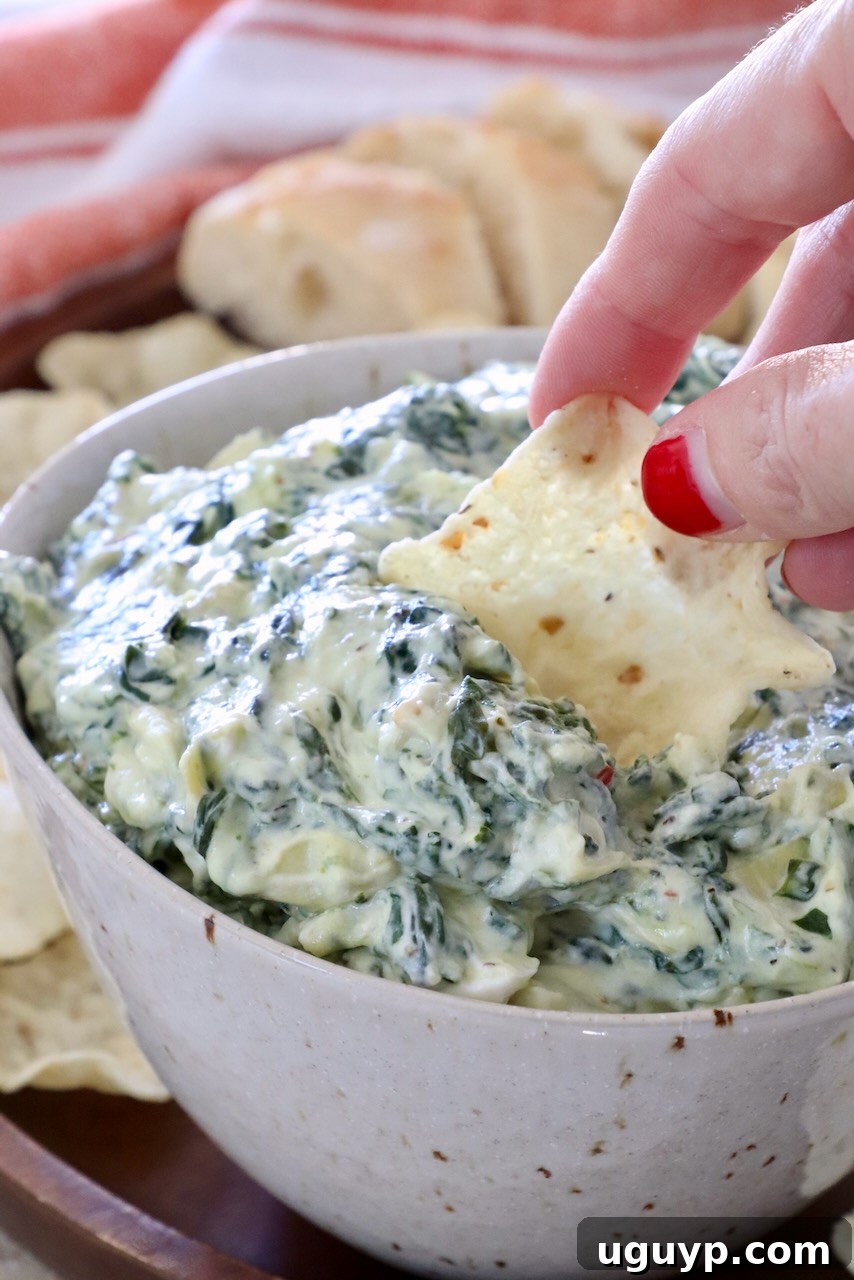 hand dipping a tortilla chip into a bowl of creamy hot spinach artichoke dip