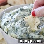 hand dipping a tortilla chip in a bowl of hot spinach artichoke dip