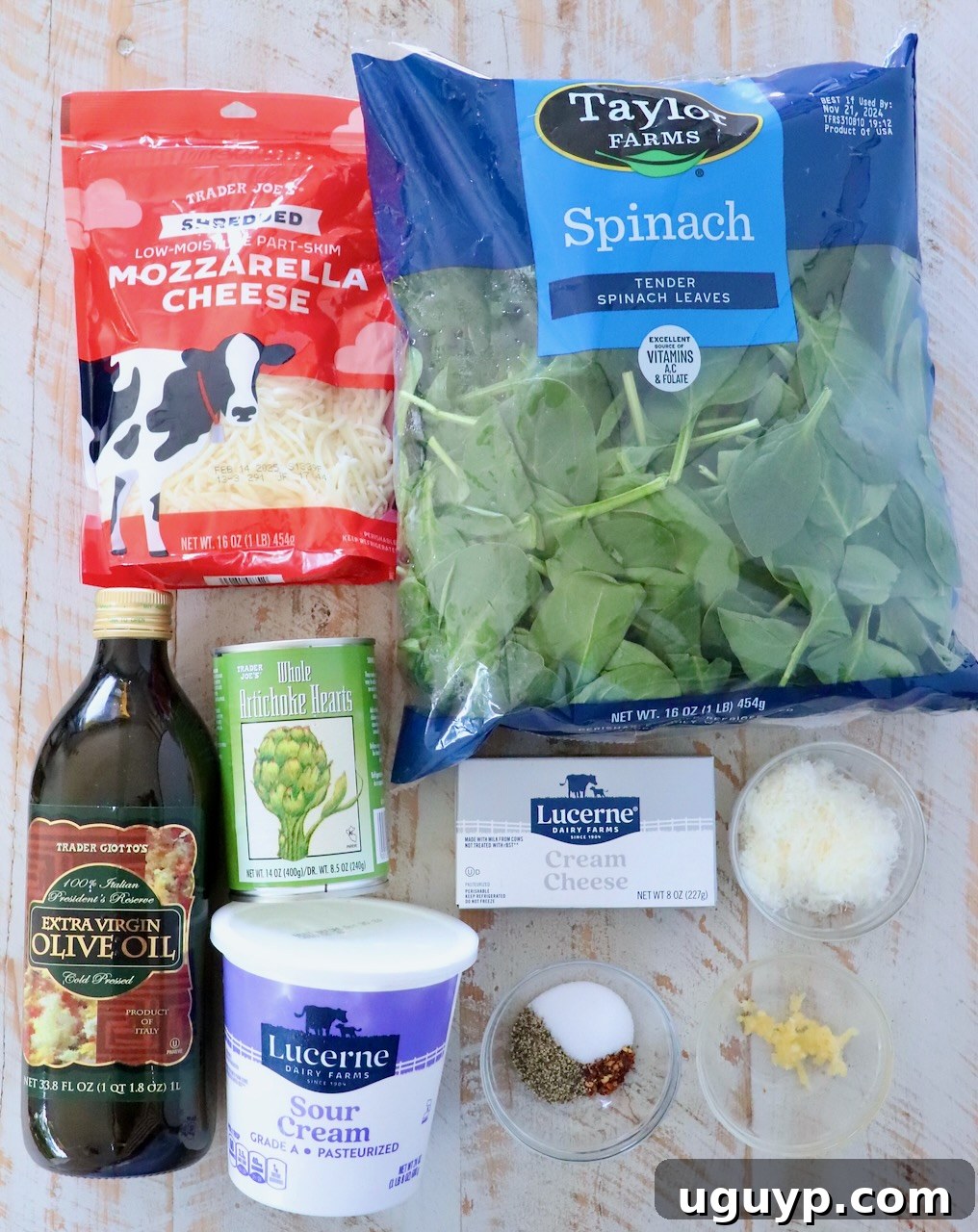 ingredients for homemade spinach artichoke dip laid out on a white wood board