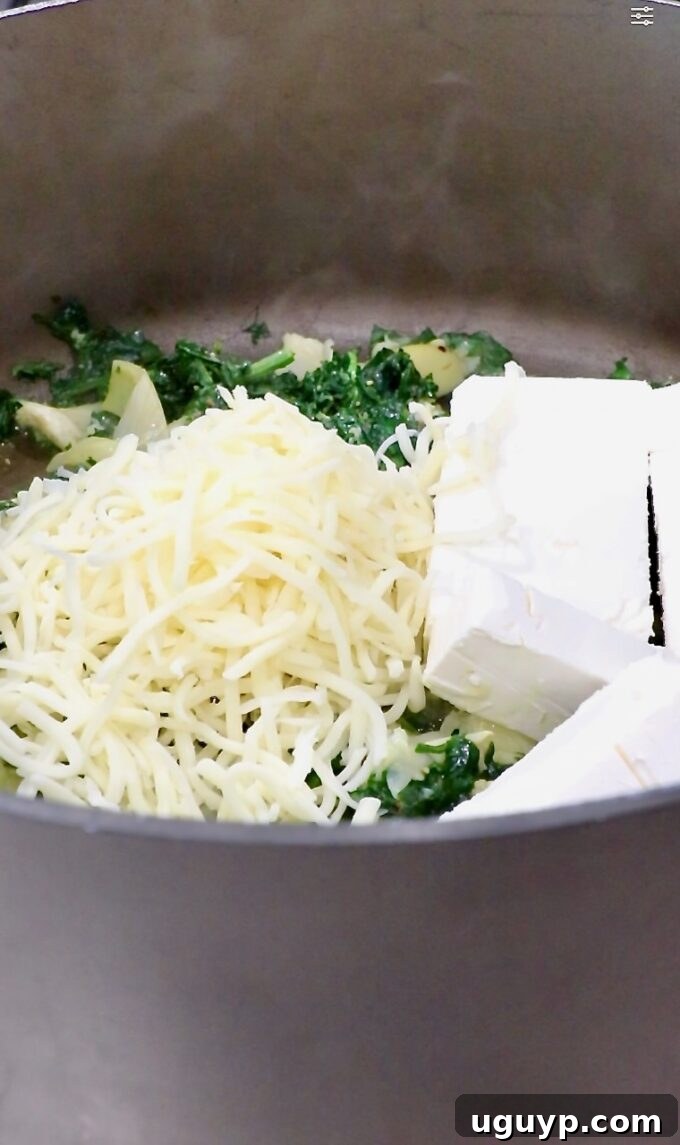 shredded mozzarella cheese and cubed cream cheese added to cooked spinach in a large pot