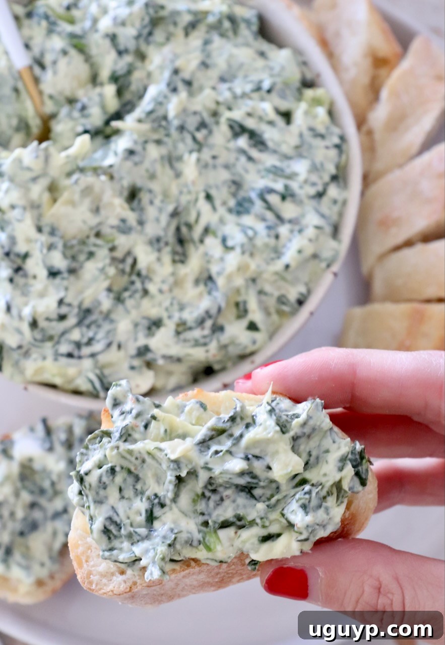 spinach artichoke dip in a bowl and spread on a slice of baguette