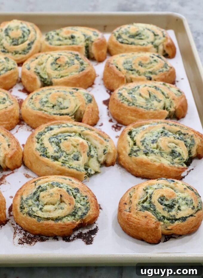 Freshly baked spinach pinwheels, golden brown and crispy, cooling on a baking sheet.