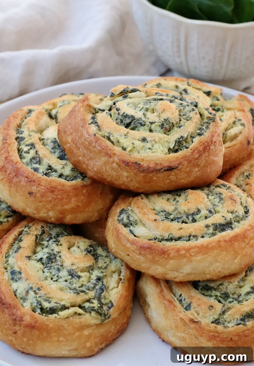 A close-up shot of several spinach rolls, beautifully stacked on a white plate, highlighting their golden crust and cheesy filling.