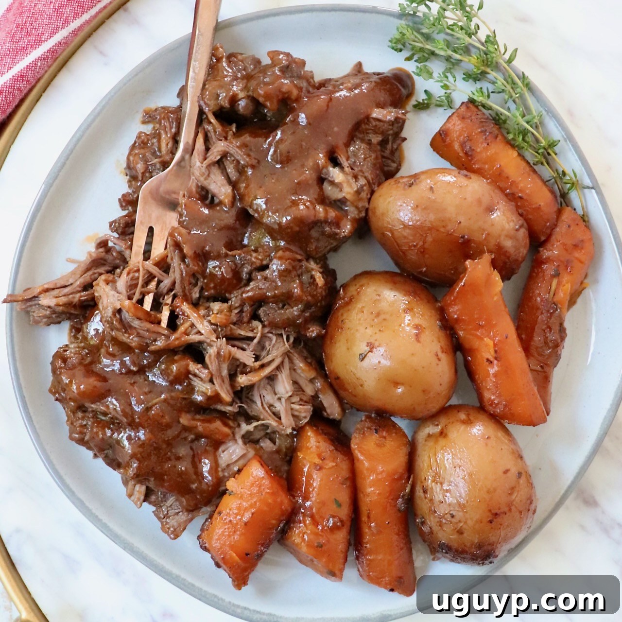 Pot roast with gravy on a plate with a fork, potatoes, and carrots