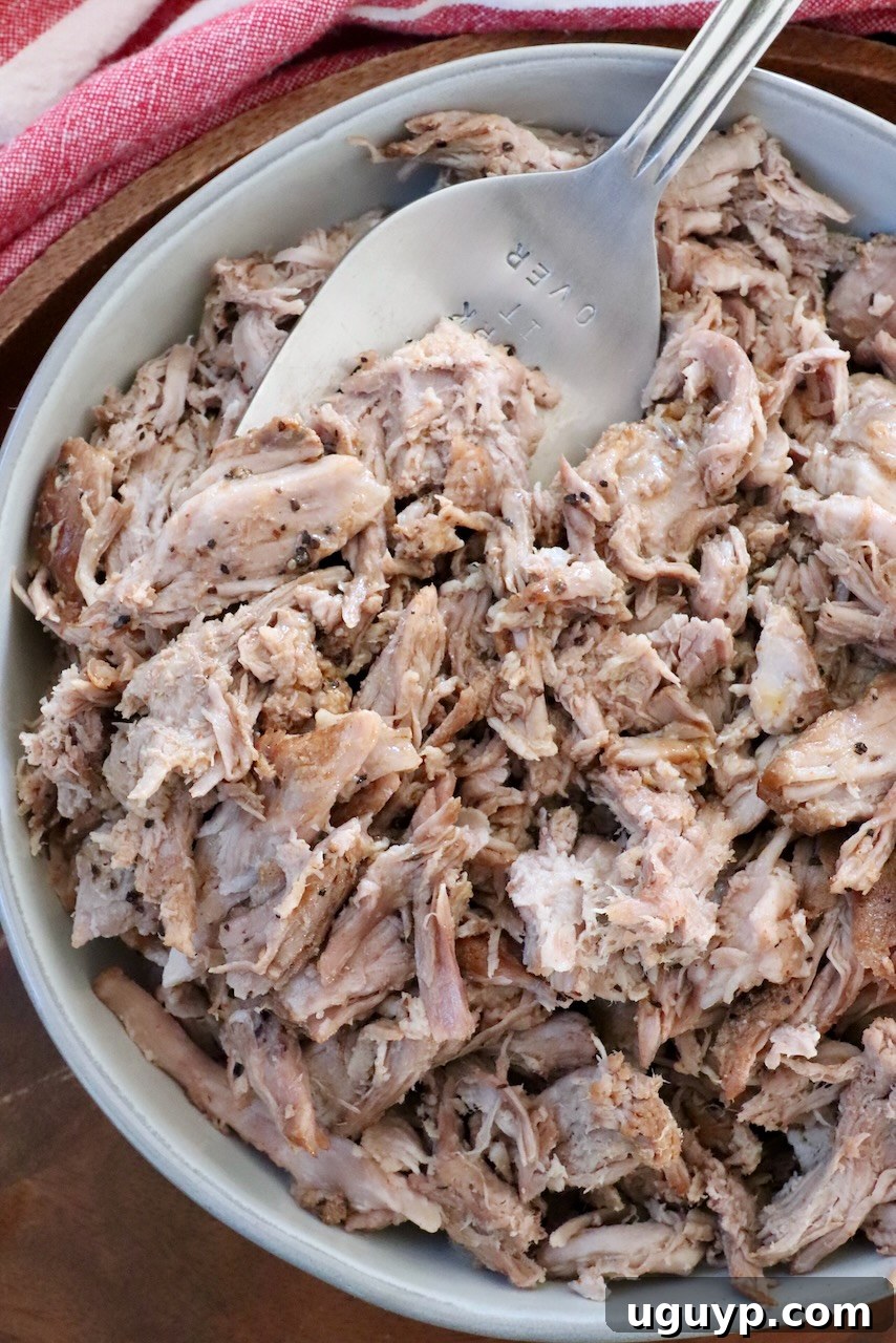 A bowl of freshly pulled pork, glistening with juices, with a large serving fork ready to scoop.