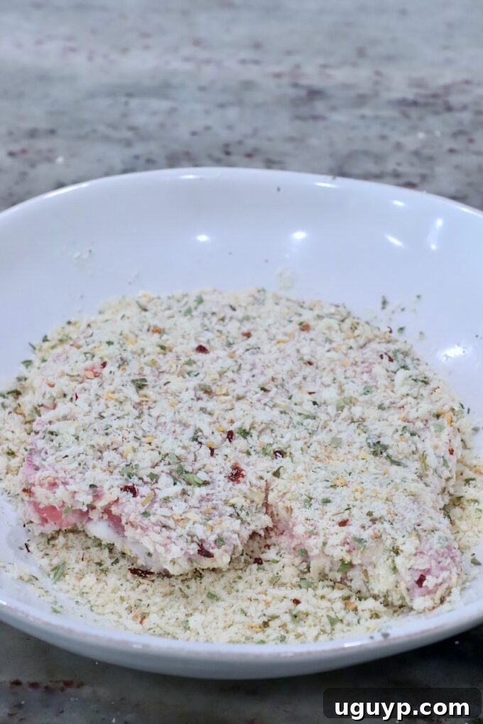 A boneless pork chop fully coated in the seasoned breadcrumb mixture, ready for pan-frying.