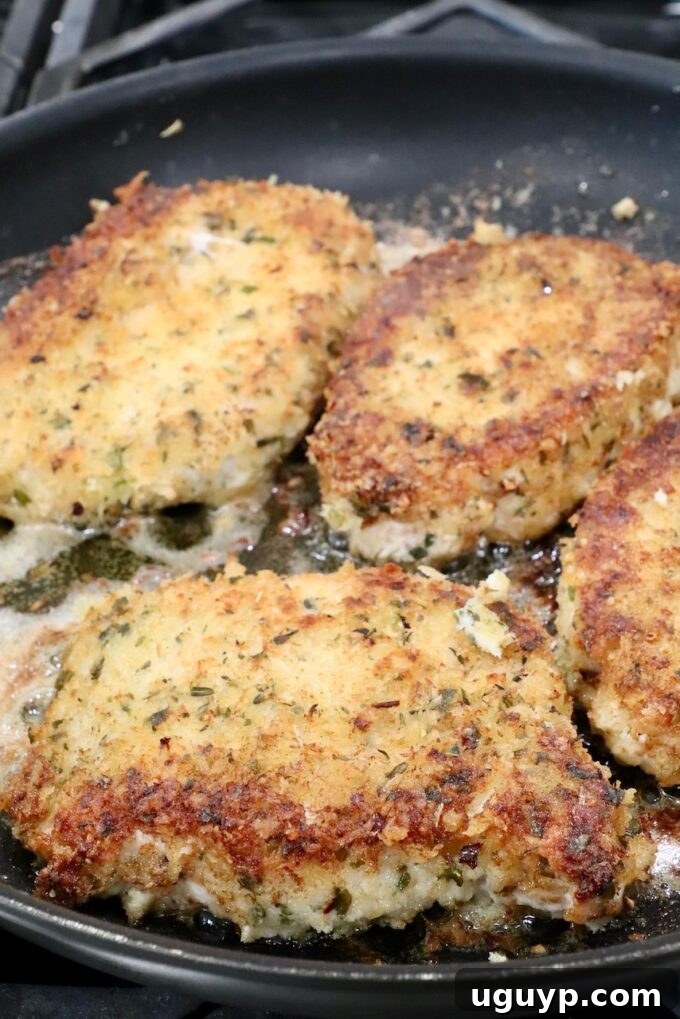 Two breaded pork chops sizzling in a large skillet with melted butter and olive oil, developing a golden-brown crust.