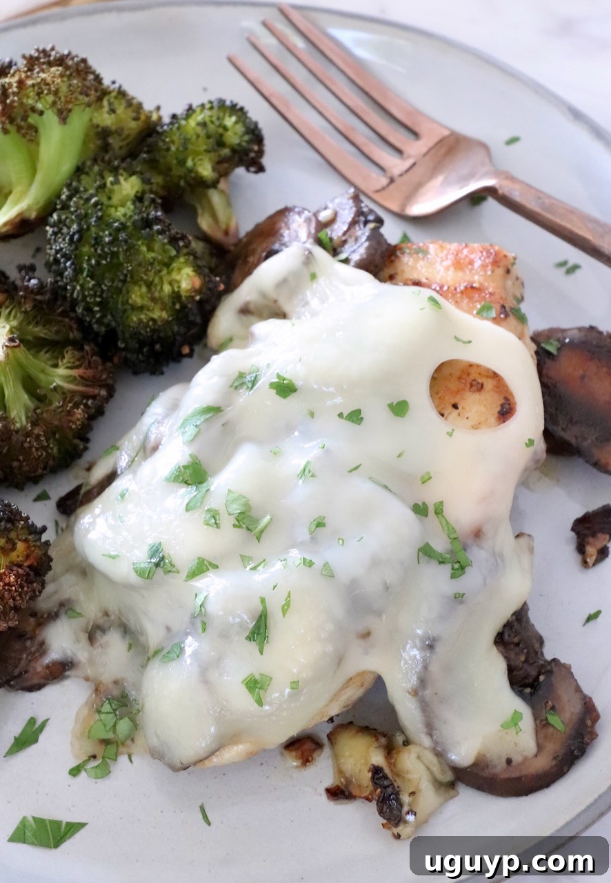 chicken topped with mushrooms and melted cheese on a plate with broccoli