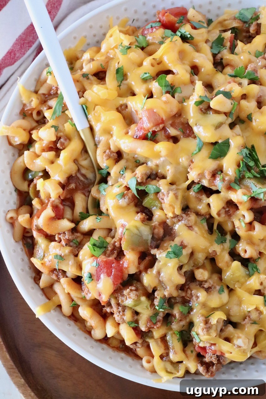 prepared goulash in a bowl with a spoon, generously covered with shredded cheddar cheese