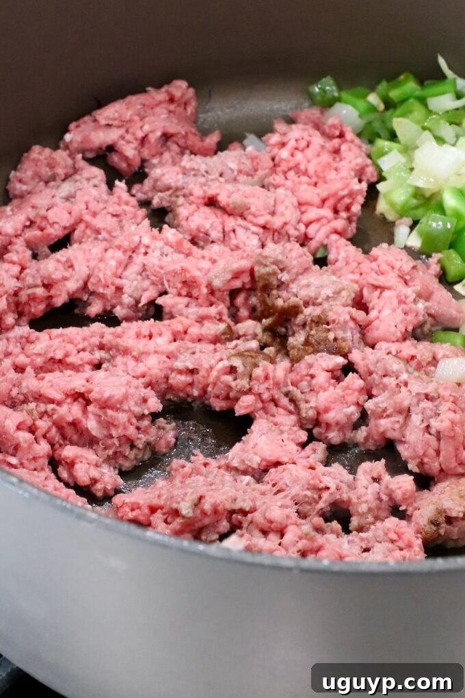 ground beef browning in a large pot with diced onions and bell peppers