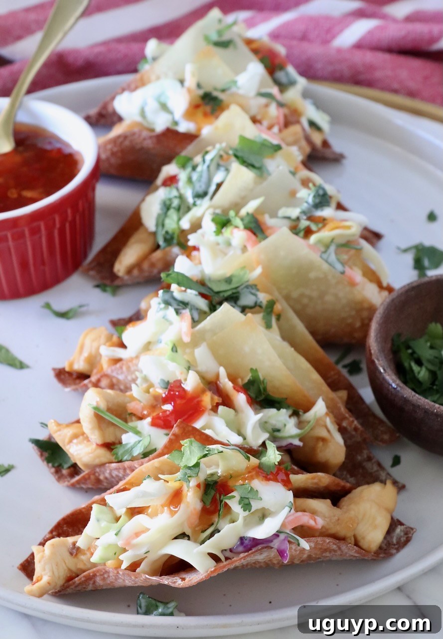 wonton tacos filled with chicken and coleslaw on a plate next to a bowl of sweet chili sauce