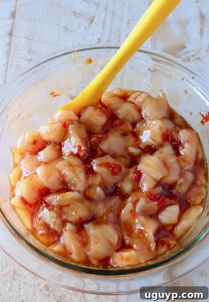 diced chicken mixed with sweet chili sauce in a glass bowl with a yellow spatula