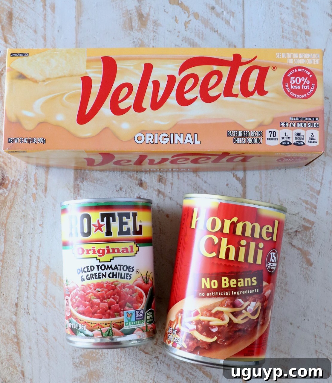 Ingredients for chili cheese dip laid out on a white wooden board, including Velveeta, Rotel, and canned chili.