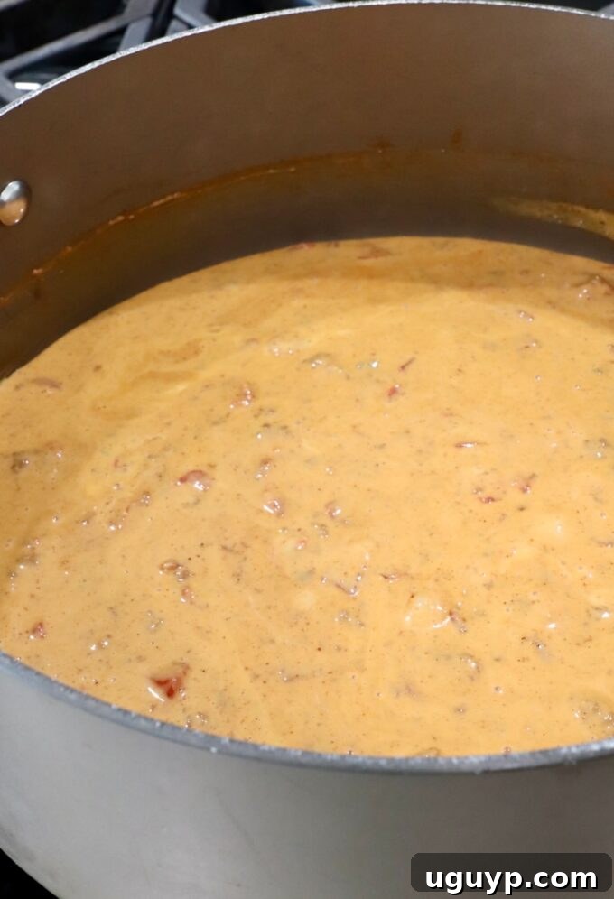 Smooth, creamy chili cheese dip simmering in a large pot on the stove.