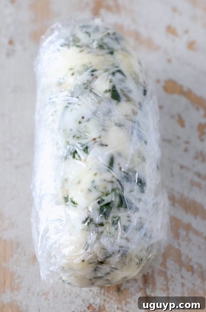 compound butter wrapped up in plastic wrap on a white wood board