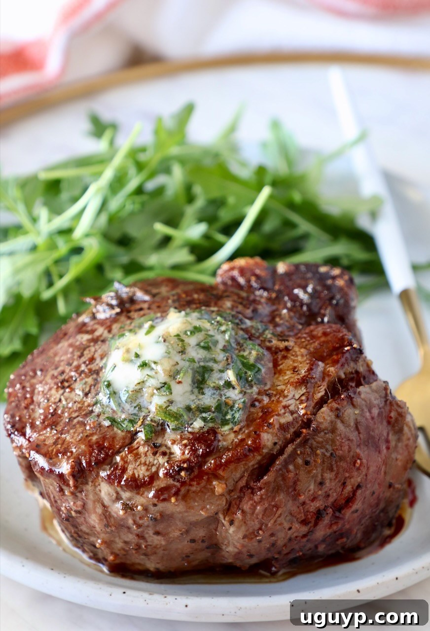 cooked steak on a plate topped with herb butter with arugula on the side of the plate