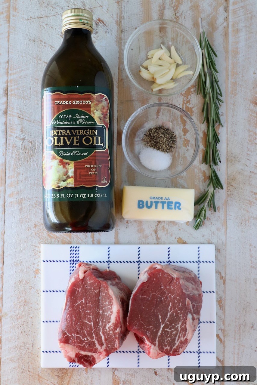 Ingredients for cooking filet mignon laid out on a white wooden board, including steak, butter, garlic, rosemary, olive oil, salt, and pepper.