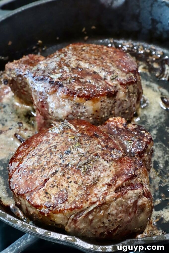 Cooked filet mignon steaks resting in a skillet, basted with aromatic garlic rosemary butter.