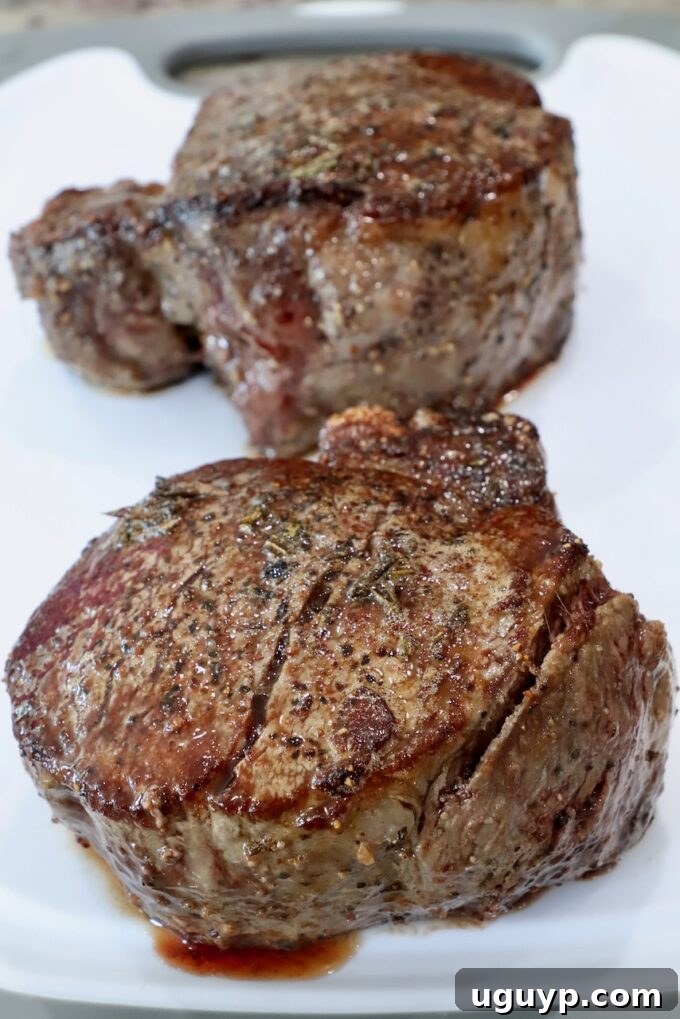 Two perfectly cooked filet mignon steaks resting on a white cutting board, ready to be sliced.