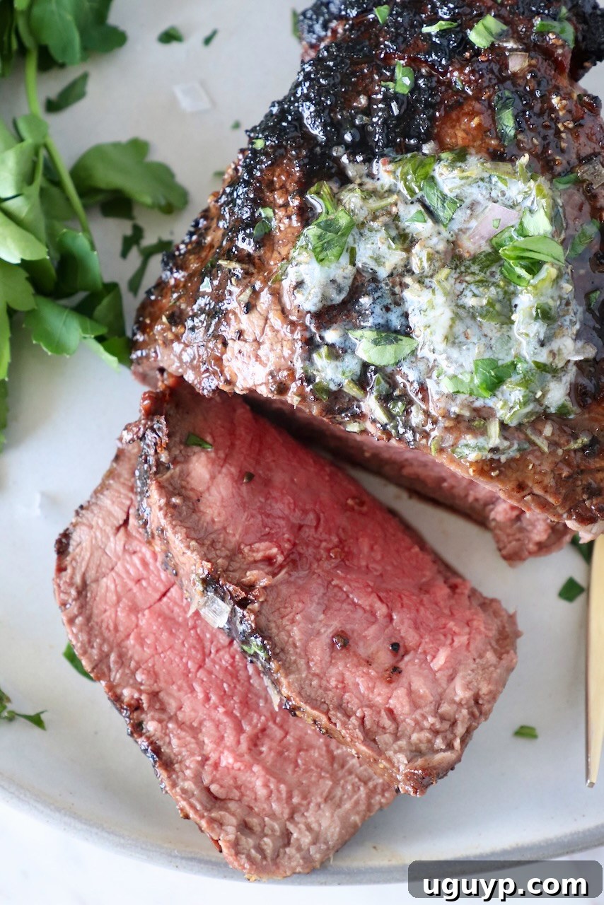 Perfectly sliced, grilled filet mignon on a plate, adorned with melted herb butter and a sprinkle of fresh parsley.