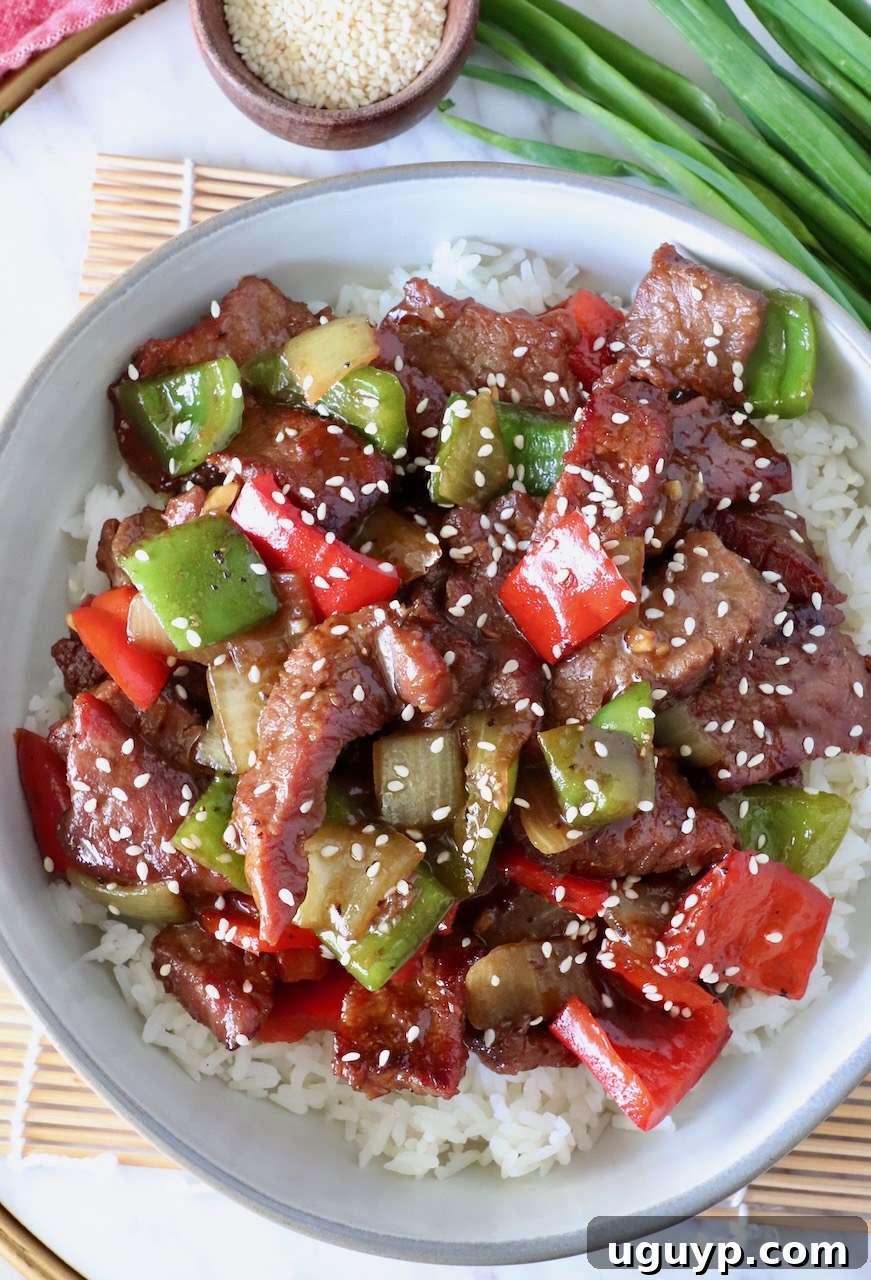 A serving of Chinese Pepper Steak Stir Fry artfully arranged over white rice in a bowl, garnished with sesame seeds.
