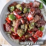 Cooked steak and peppers in sauce over cooked white rice in a bowl, topped with sesame seeds.