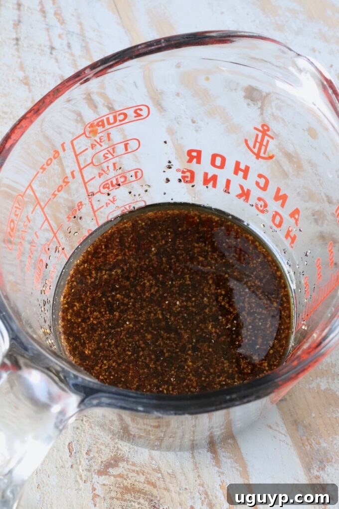 A rich black pepper sauce, prepared and whisked in a glass measuring cup, showcasing its deep, savory color.