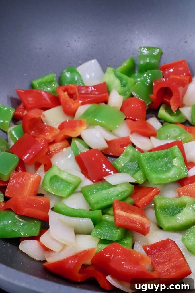 Vibrantly colored diced bell peppers and onions cooking in a large wok, beginning to soften and caramelize.