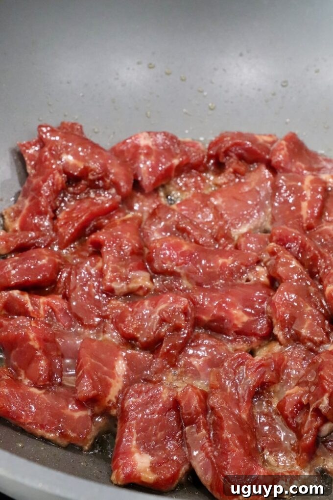 Marinated strips of uncooked flank steak searing in a hot wok, creating a beautiful crust.