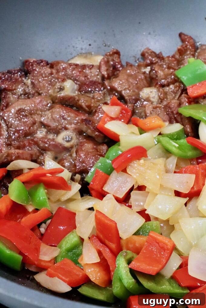 Cooked beef, bell peppers, and onions combined in a large wok, ready for the flavorful sauce.