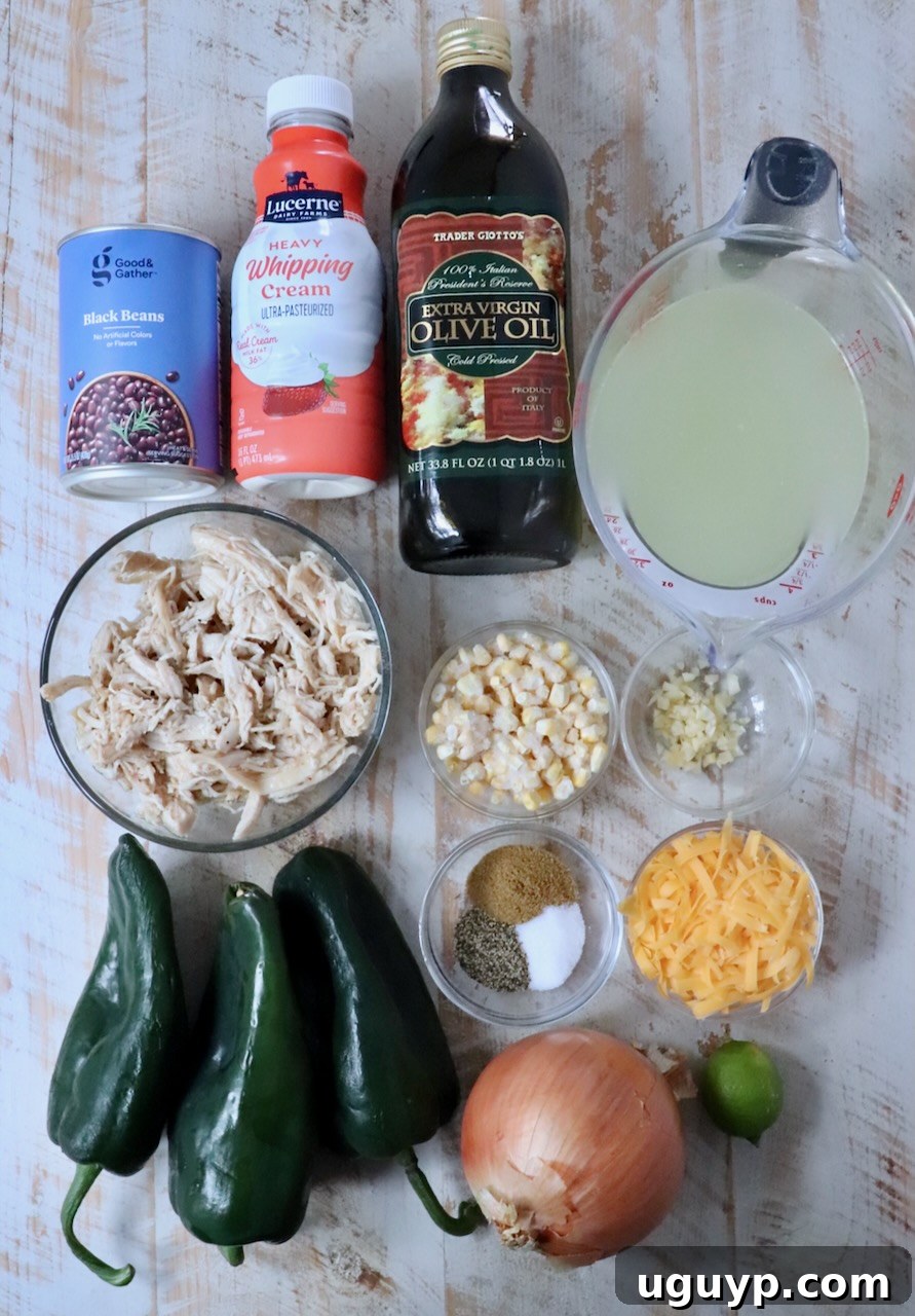 A colorful array of fresh ingredients for Chicken Poblano Soup, including poblano peppers, corn, black beans, onions, garlic, and shredded chicken, neatly arranged on a white wooden board.