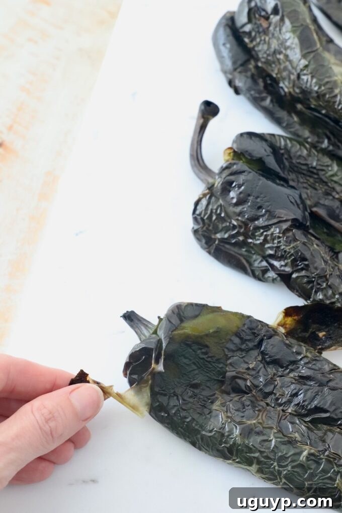 A hand gently peeling the charred skin from a roasted poblano pepper on a cutting board, revealing the tender flesh beneath.