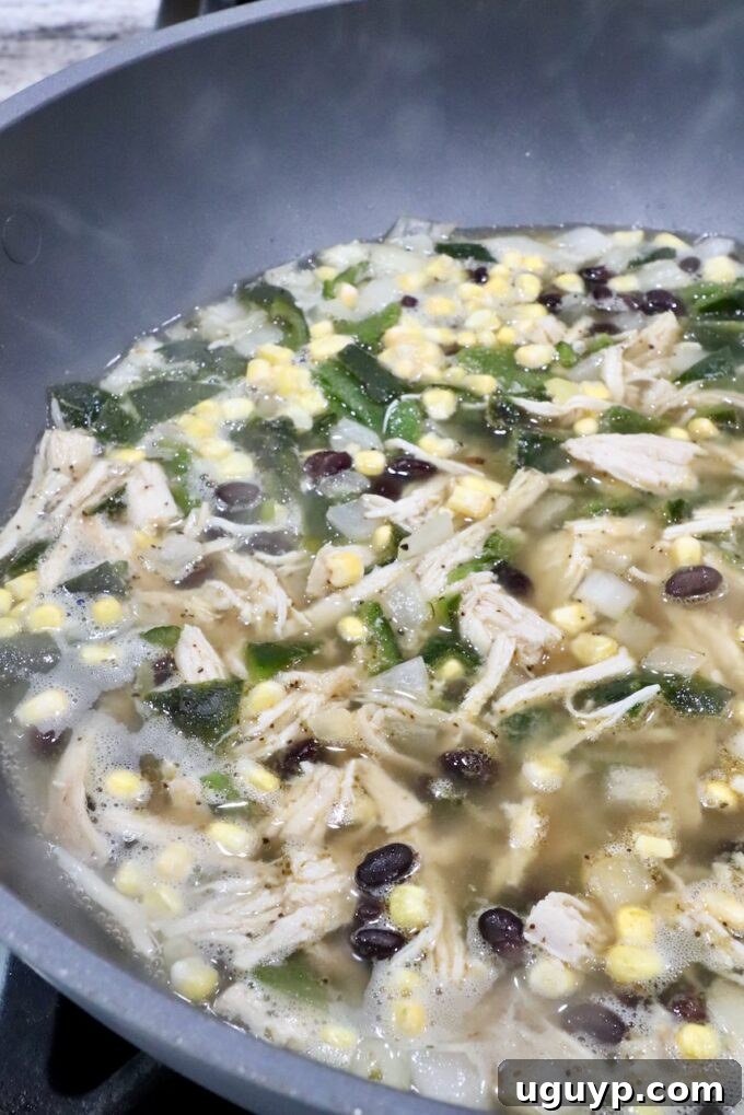 Chicken Poblano Soup simmering in a large pot on the stove, with all ingredients combined in a flavorful broth.